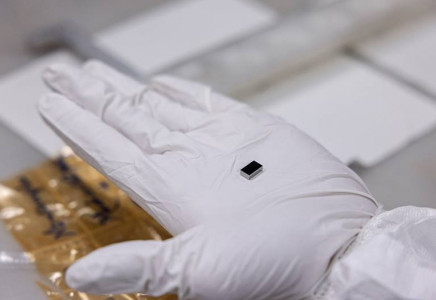 A small rectangular piece of niobium sits in the middle of someone's palm, which is fitted with a white glove.