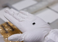 A small rectangular piece of niobium sits in the middle of someone's palm, which is fitted with a white glove.