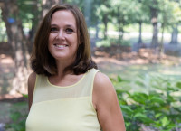Clair Papas head & shoulders portrait in yellow shirt, trees in background