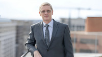 Sean Hearne, AAAS Fellow, in a business suit standing outdoors with a cityscape in the background.
