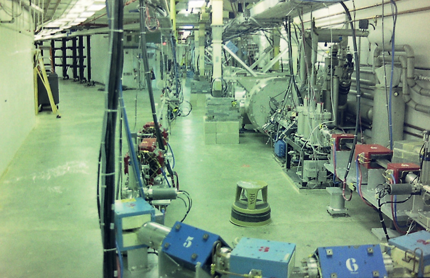 A scale model of the Continuous Electron Beam Accelerator Facility, with blue magnets surrounding a steel beamline, is illuminated inside the accelerator tunnel.