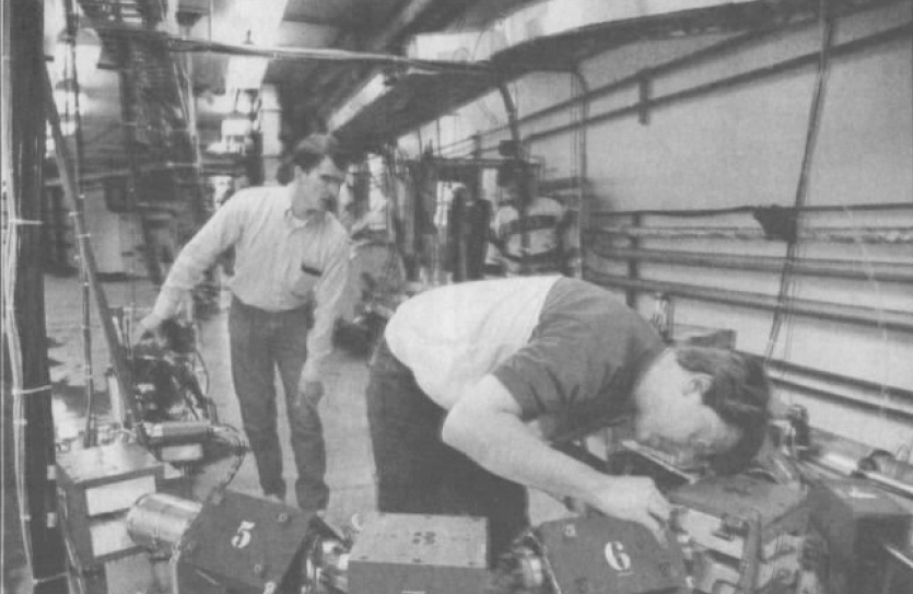 A black-and-white newspaper photo from 1991 shows Nick Sereno checking magnets on small version of the Continuous Electron Beam Accelerator Facility's racetrack-shaped beamline